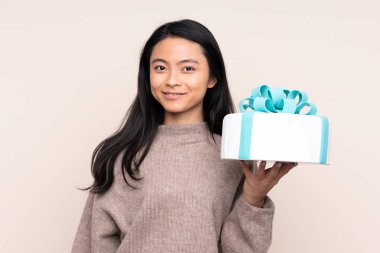 Genç Asyalı bir kız elinde büyük bir pasta tutuyor. Bej arka planda izole edilmiş, gülümsüyor.