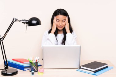 İş yerinde bej arka planda başağrısı olan bilgisayarlı Asyalı öğrenci.