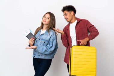 Mavi arka planda izole edilmiş bir bavul taşıyan gezgin çift geriye bakıyor ve bir ürün sunuyorlar.