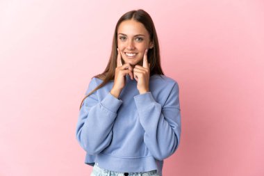 Soyutlanmış pembe arka planı olan genç bir kadın mutlu ve hoş bir ifadeyle gülümsüyor.