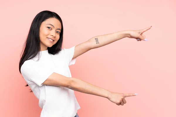 Teenager Chinese woman isolated on pink background pointing finger to the side and presenting a product