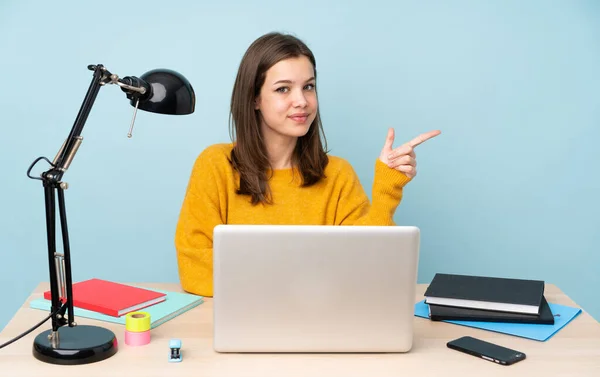 Student girl studying in her house isolated on blue background pointing finger to the side