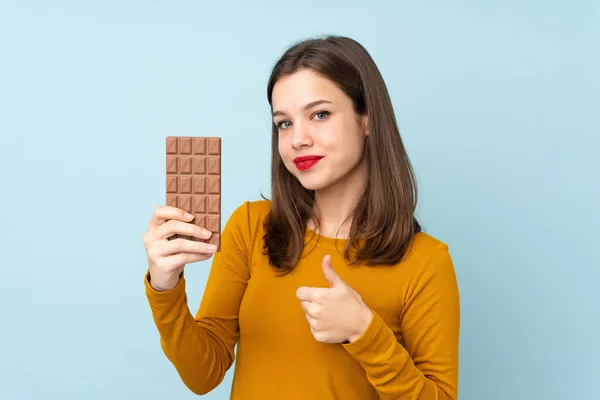 Teenager Girl Isolated Blue Background Taking Chocolate Tablet Thumb — Stock Photo, Image