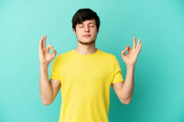 Genç Rus adam Zen pozunda mavi arka planda izole edildi.