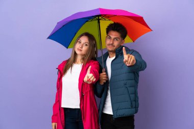 Mavi arka planda şemsiye tutan çift parmağını kaldırıyor ve gösteriyor.