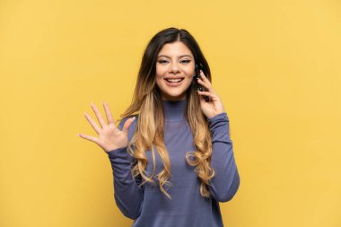 Sarı arka planda izole edilmiş cep telefonu kullanan genç Rus kız parmaklarıyla beşi sayıyor.
