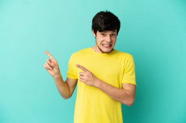 Genç Rus adam mavi arka planda izole edilmiş korkmuş ve kenarı işaret ediyor.