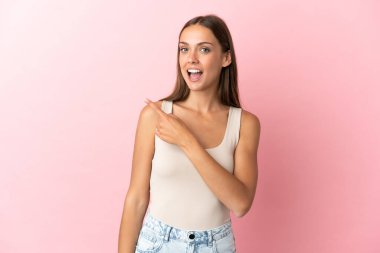 Soyutlanmış pembe arka planı olan genç bir kadın şaşırmış ve işaret ediyor.