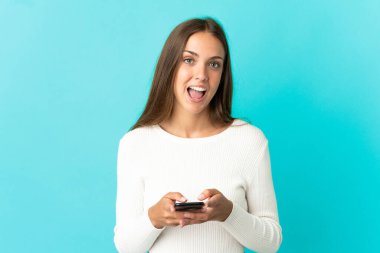 İzole edilmiş mavi arka planı olan genç bir kadın şaşırdı ve bir mesaj gönderiyor.