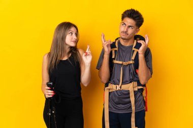 Sarı arka planda izole edilmiş büyük sırt çantalı genç dağcı çift şans diliyor.