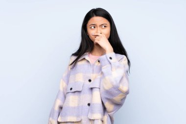 Genç Çinli bir kadın mavi arka planda izole edilmiş. Şüpheleri var ve kafası karışmış bir yüz ifadesi var.