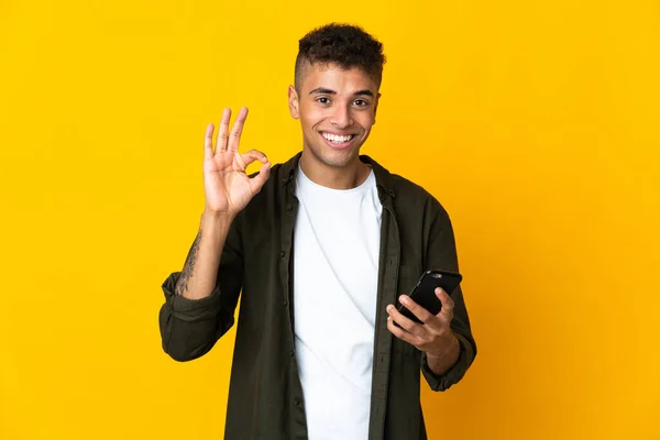 Młody Brazylijczyk Odizolowany Żółtym Tle Pomocą Telefonu Komórkowego Robi Znak — Zdjęcie stockowe