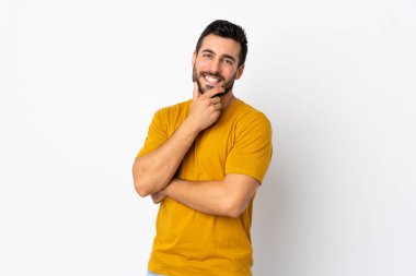 Beyaz arka planda sakallı yakışıklı genç adam mutlu ve gülümsüyor.