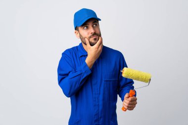 Boyacı beyaz arka planda izole edilmiş bir boya silindiri tutuyor. Şüpheleri var ve kafası karışmış bir yüz ifadesi var.