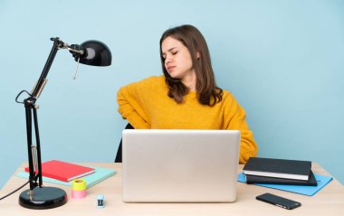 Öğrenci kız, mavi arka planda izole bir şekilde evinde ders çalışıyor. Çabaladığı için sırt ağrısı çekiyor.