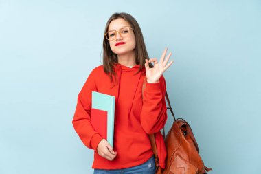 Mavi arka planda izole edilmiş kitapları tutan öğrenci kız parmaklarıyla 