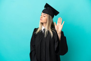 İzole edilmiş mavi arka planda genç üniversite mezunu stop jest yapıyor ve hayal kırıklığına uğruyor