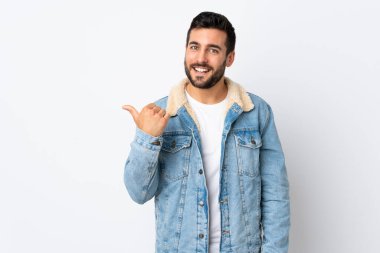 Beyaz arka planda sakallı yakışıklı genç bir adam bir ürün sunmak için kenarı işaret ediyor.