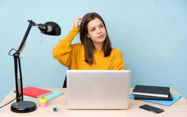 Öğrenci kız evinde çalışıyor. Mavi arka planda izole halde. Kafasını kaşırken şüpheleri var.