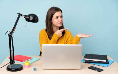 Evinde okuyan öğrenci kız, mavi arka planda izole edilmiş bir şekilde avucunun içinde hayali bir ilan tutuyor.