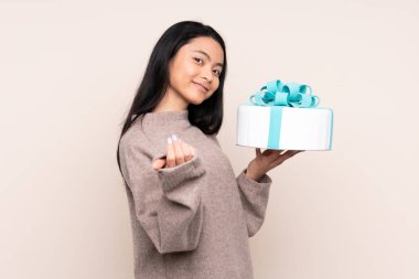 Genç Asyalı kız elinde bej arka planda izole edilmiş büyük bir pasta tutuyor. Bizimle gelmesi için davet ediyor. Gelmene sevindim.