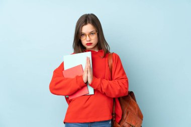 Öğrenci kız elinde kitaplarla mavi arka planda yalvarıyor