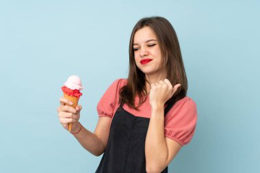 Kornet dondurması tutan genç kız mavi arka planda izole bir şekilde zaferi kutluyor.