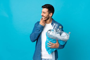 Elinde plastik şişelerle dolu bir çanta tutan beyaz bir adam mavi arka planda izole edilmiş bir şekilde duruyor.