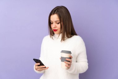 Mor arka planda izole edilmiş genç bir kız elinde kahve ve cep telefonu var.