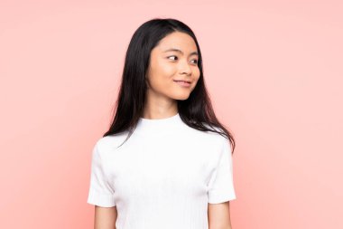 Genç Çinli bir kadın pembe arka planda izole edilmiş, yan tarafa bakıyor ve gülümsüyor.