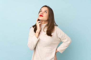 Genç kız mavi arka planda izole edilmiş bir fikir düşünüyor.