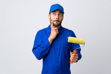 Boyacı beyaz arka planda izole edilmiş bir boya silindiri tutuyor. Şüpheleri ve düşünceleri var.