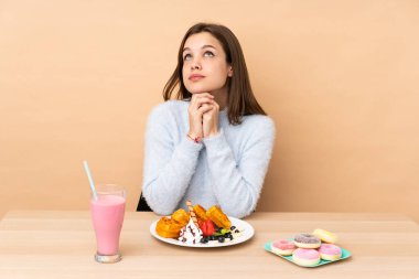 Bej arka planda izole edilmiş waffle yiyen genç bir kız.