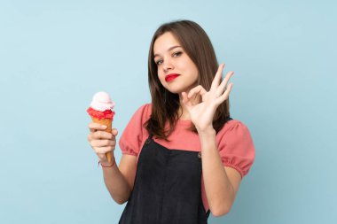Kornet dondurması tutan genç kız mavi arka planda izole edilmiş. Parmaklarıyla işaret veriyor.
