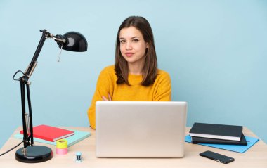 Öğrenci kız, mavi arka planda izole bir şekilde evinde çalışıyor. Kollarını ön cephede kavuşturuyor.