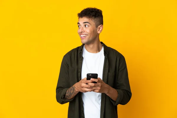 Joven Brasileño Aislado Sobre Fondo Amarillo Usando Teléfono Móvil Mirando — Foto de Stock