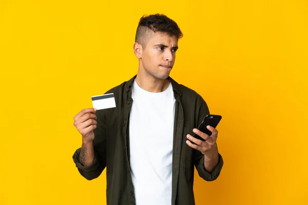 Νεαρός Βραζιλιάνος Απομονωμένος Κίτρινο Φόντο Αγοράζει Κινητό Πιστωτική Κάρτα Ενώ — Φωτογραφία Αρχείου