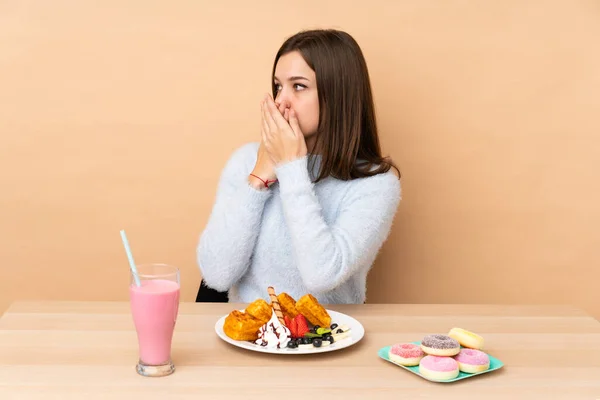 Chica Adolescente Comiendo Gofres Aislados Sobre Fondo Beige Cubriendo Boca —  Fotos de Stock