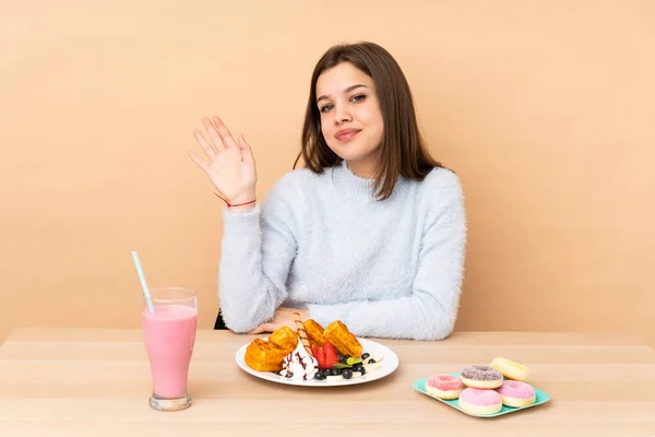 Chica Adolescente Comiendo Gofres Aislados Sobre Fondo Beige Saludando Con — Foto de Stock