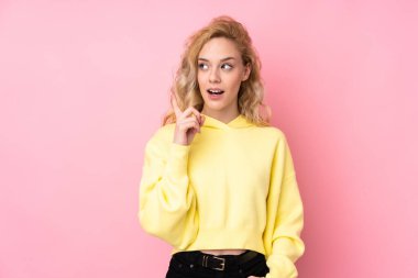 Pembe arka planda izole edilmiş bir tişört giyen genç sarışın kadın, bir fikrin parmağıyla işaret ettiğini düşünüyor.