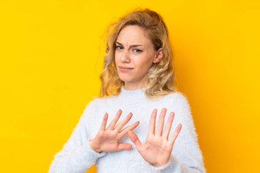 Sarı arka planda izole edilmiş genç sarışın kadın gergin ellerini öne uzatıyor.