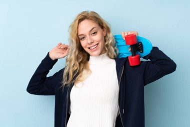 Genç sarışın kadın mavi arka planda tek başına paten kayıyor.