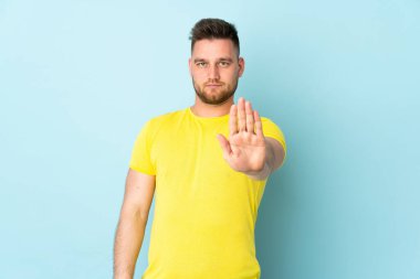 Mavi arka planda izole edilmiş Rus yakışıklı adam dur hareketi yapıyor.