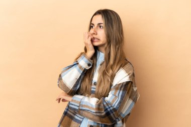 Bej arka planda izole edilmiş genç beyaz kadın biraz gergin.