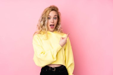 Pembe arka planda izole edilmiş, süveter giyen genç sarışın kadın şaşırmış ve işaret ediyor.