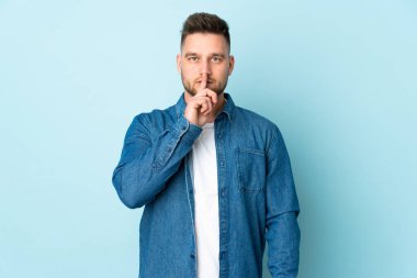 Mavi arka planda izole edilmiş Rus yakışıklı bir adam sessizlik işareti gösteriyor. Parmağını ağzına sokuyor.