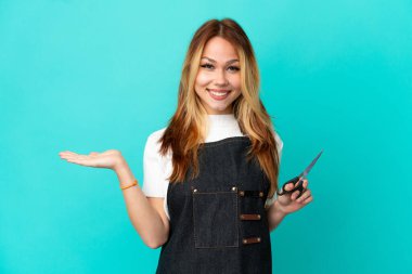 İzole edilmiş mavi arka plan üzerinde genç kuaför kız bir ilan vermek için avuç içinde hayali bir fotokopi makinesi tutuyor.