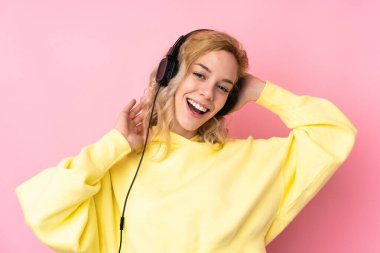 Pembe arka planda izole edilmiş sweatshirt giyen genç sarışın kadın müzik dinliyor.