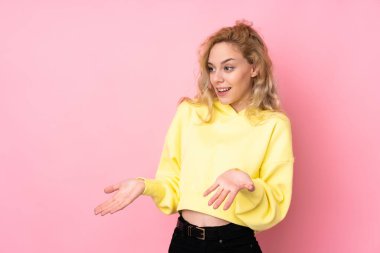 Pembe arka planda izole edilmiş, süveter giyen genç sarışın bir kadın.
