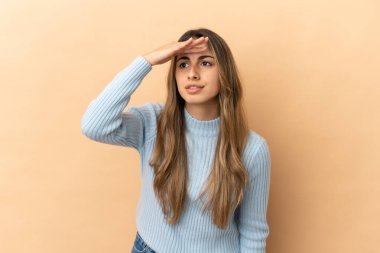 Beyazlı genç bir kadın bej arka planda izole edilmiş. Bir şeye bakmak için uzaklara bakıyor.